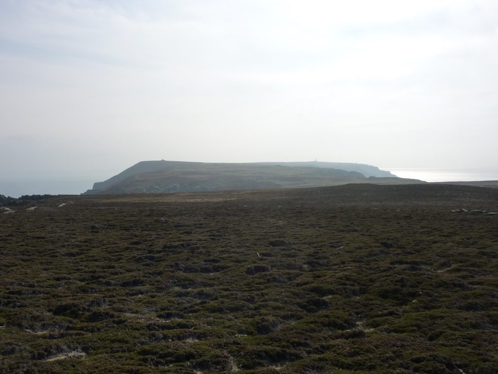 Picture of a wide moor like landscape with two buildings in the far distance and the sea either side