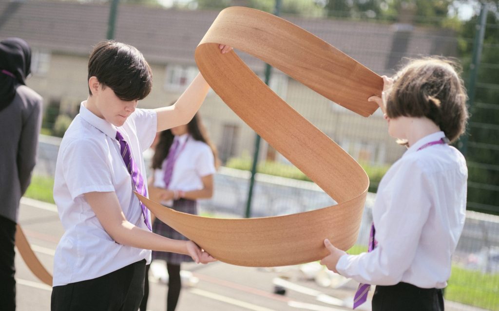 Two school pupils working with thin strip of wood to create helix shape