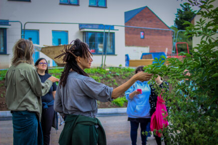 Artist Kayle Brandon reaching out for a plant at Roseneath Gardens with a group of people